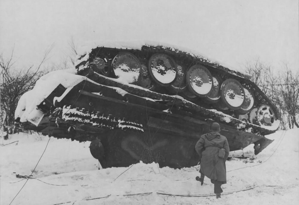 A US Air Force officer in winter clothing examines an overturned German Panther tank abandoned in the Ardennes, January 1945.