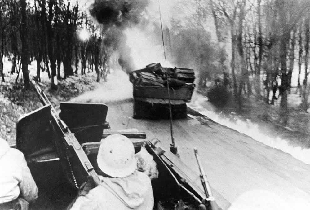 A black-and-white photo of a German armored halftrack approaching a burning Soviet truck during the German attamtps to relieve the besieged garrison of Budapest in January 1945