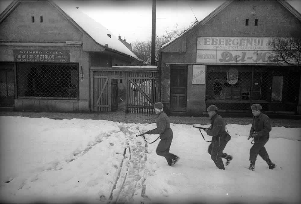 A black-and-white photo of three Soviet soldiers, holding their rifles, walking on a snowy street in Budapest, January 1945.